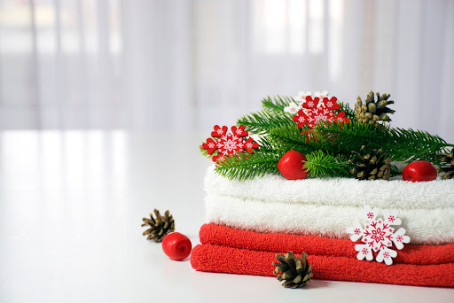 Fresh red and white towels folded on the table, fir branches, snowflakes and pine cones with tulle window on background. New year cozy home interior. Christmas spa or beauty salon concept. Copy space